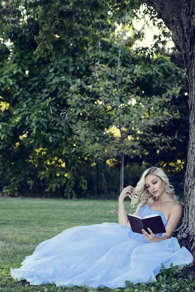 Kvinna i blå klänning en bok som lutar på träd — Stockfoto