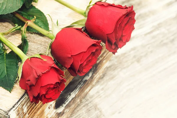 Three red roses on wooden desk — Stock Photo, Image