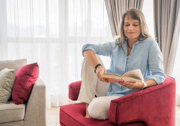 Μια Ώριμη Γυναίκα Διαβάζει Ένα Βιβλίο Στο Αστικό Της Διαμέρισμα — Φωτογραφία Αρχείου