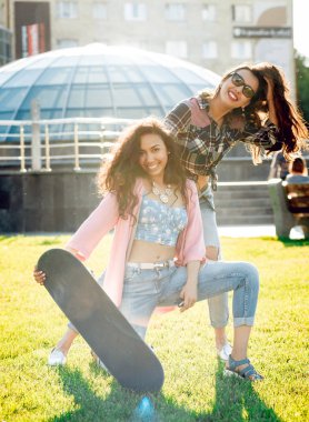 Yeşil çimenlerin üzerinde poz kaykay ile rahat kıyafetler'de iki genç karışık yarış kız