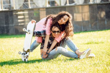 Yeşil çimenlerin üzerinde poz kaykay ile rahat kıyafetler'de iki genç karışık yarış kız