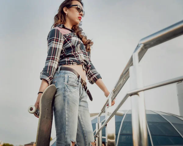 Güzel dalgalı saçlı öpebileceğinize kız açık havada kaykay ile poz Kareli gömlekli