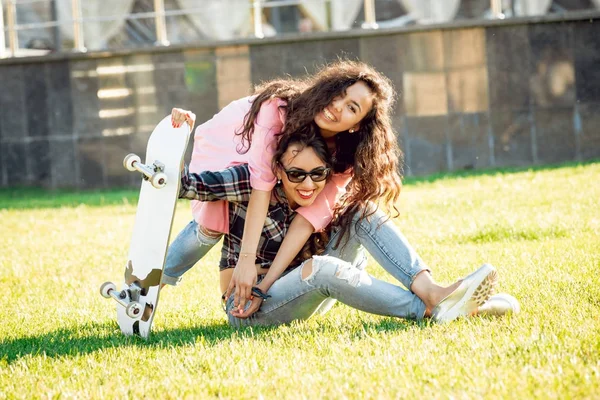 Yeşil çimenlerin üzerinde poz kaykay ile rahat kıyafetler'de iki genç karışık yarış kız