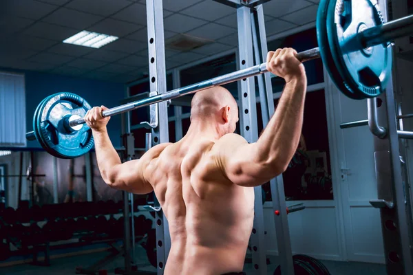 Spor salonunda halterle egzersiz yapan kaslı bir adam.