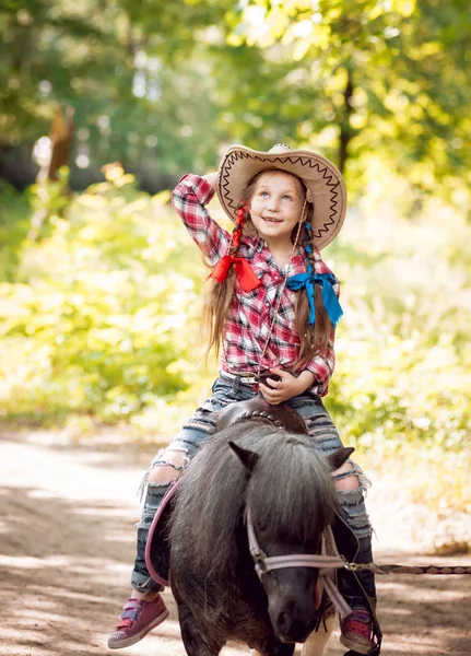 小女孩与辫子在牛仔帽骑小马在公园 — 图库照片