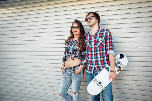 Young couple with skateboard against rolling gates