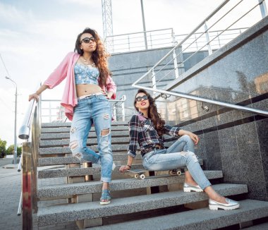 İki genç karışık yarış kız rahat kıyafetler ile kaykay sokakları etrafında yürüyüş içinde