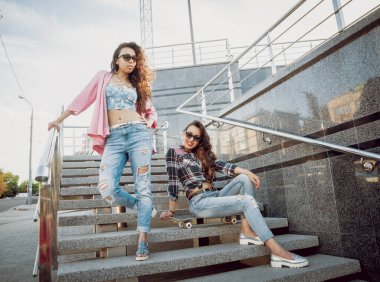 İki genç kız açık havada kaykay ile poz