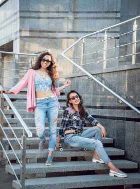 İki genç karışık yarış kız rahat kıyafetler ile kaykay sokakları etrafında yürüyüş içinde