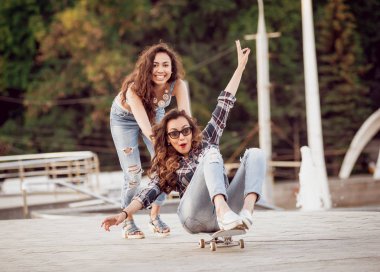 İki genç kız açık havada kaykay ile eğleniyor