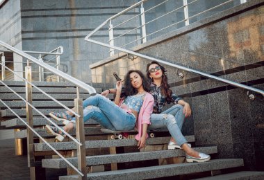 İki genç karışık yarış kız rahat kıyafetler ile kaykay sokakları etrafında yürüyüş içinde