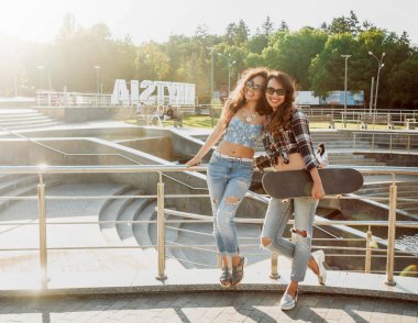 İki genç karışık yarış kız rahat kıyafetler ile kaykay sokakları etrafında yürüyüş içinde