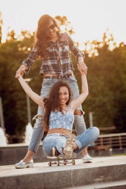 İki genç kız açık havada kaykay ile eğleniyor