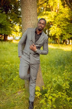 Park ağaç yakınındaki gri elbiseli genç Afrika adam