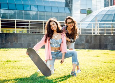 Yeşil çimenlerin üzerinde poz kaykay ile rahat kıyafetler'de iki genç karışık yarış kız