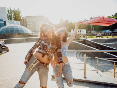 İki genç karışık yarış kız rahat kıyafetler ile kaykay sokakları etrafında yürüyüş içinde