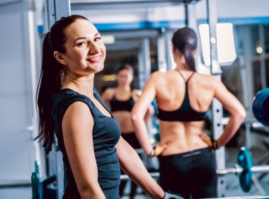 İki esmer kadın spor salonunda egzersizleri yapıyor.