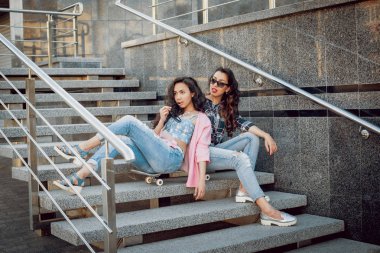 İki genç karışık yarış kız rahat kıyafetler ile kaykay sokakları etrafında yürüyüş içinde