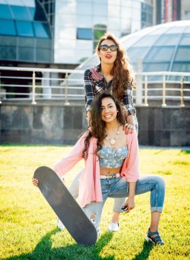 Yeşil çimenlerin üzerinde poz kaykay ile rahat kıyafetler'de iki genç karışık yarış kız