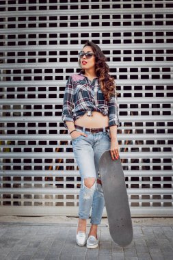 Güzel dalgalı saçlı öpebileceğinize kız açık havada kaykay ile poz Kareli gömlekli