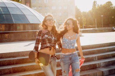 İki genç karışık yarış kız rahat kıyafetler ile kaykay sokakları etrafında yürüyüş içinde