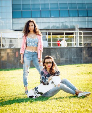 Yeşil çimenlerin üzerinde poz kaykay ile rahat kıyafetler'de iki genç karışık yarış kız