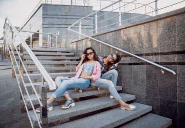 İki genç karışık yarış kız rahat kıyafetler ile kaykay sokakları etrafında yürüyüş içinde