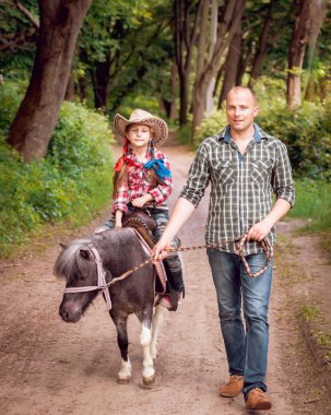 Kovboy şapkası binme midilli küçük kız babasıyla Park