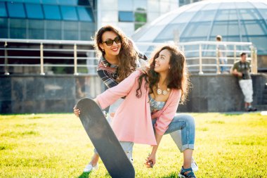 Yeşil çimenlerin üzerinde poz kaykay ile rahat kıyafetler'de iki genç karışık yarış kız