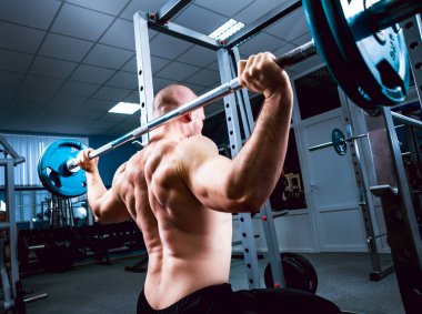 Spor salonunda halterle egzersiz yapan kaslı bir adam.