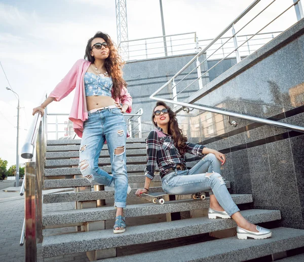 İki genç karışık yarış kız rahat kıyafetler ile kaykay sokakları etrafında yürüyüş içinde