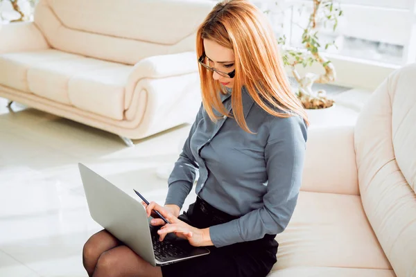 Gözlüklü genç işkadını ofiste dizüstü bilgisayar ile.