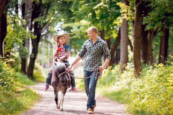 小女孩在牛仔帽骑小马与她的父亲在公园 — 图库照片