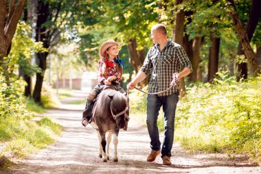 Kovboy şapkası binme midilli küçük kız babasıyla Park