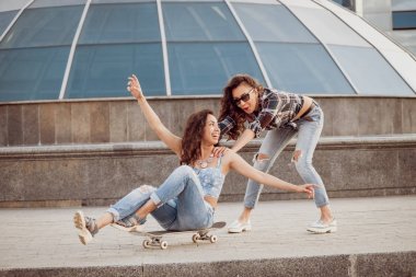 İki genç kız açık havada kaykay ile eğleniyor