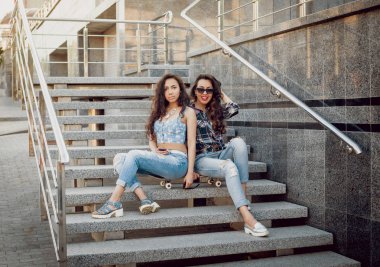 İki genç karışık yarış kız rahat kıyafetler ile kaykay sokakları etrafında yürüyüş içinde