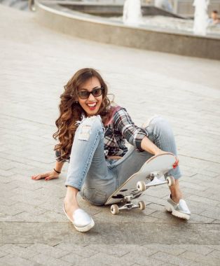 Güzel dalgalı saçlı öpebileceğinize kız açık havada kaykay ile poz Kareli gömlekli