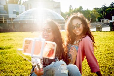 İki genç karışık yarış kız rahat kıyafetler selfie yeşil çim üzerinde yapıyor