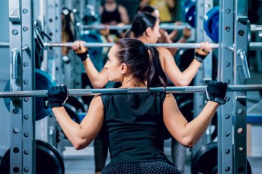 İki esmer kadın spor salonunda egzersizleri yapıyor.