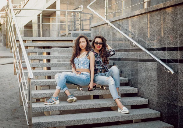 İki genç karışık yarış kız rahat kıyafetler ile kaykay sokakları etrafında yürüyüş içinde