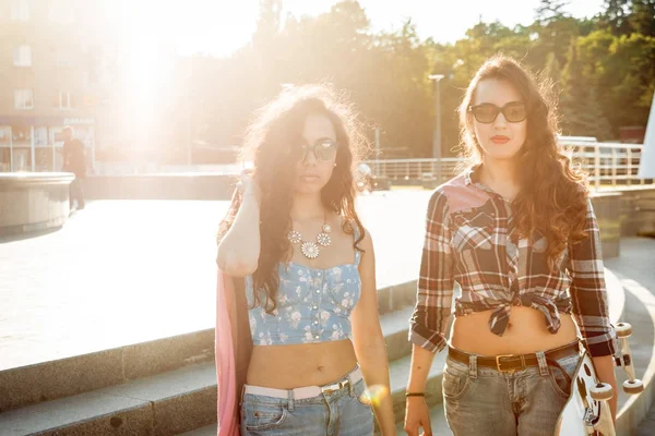 İki genç karışık yarış kız rahat kıyafetler ile kaykay sokakları etrafında yürüyüş içinde