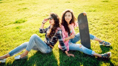 Yeşil çimenlerin üzerinde poz kaykay ile rahat kıyafetler'de iki genç karışık yarış kız