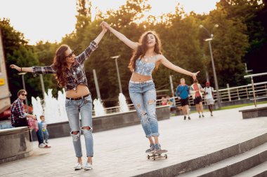 İki genç kız açık havada kaykay ile eğleniyor