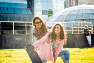 Yeşil çimenlerin üzerinde poz kaykay ile rahat kıyafetler'de iki genç karışık yarış kız