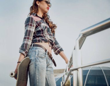 Güzel dalgalı saçlı öpebileceğinize kız açık havada kaykay ile poz Kareli gömlekli