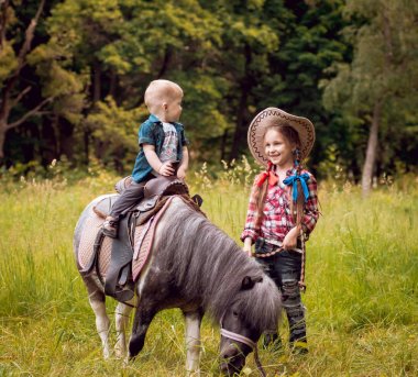 Küçük kız ve at binme erkek kardeşi yeşil park midilli