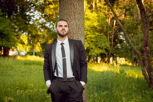 Park ağaç yakınındaki kravat ile siyah elbiseli adam genç sakallı