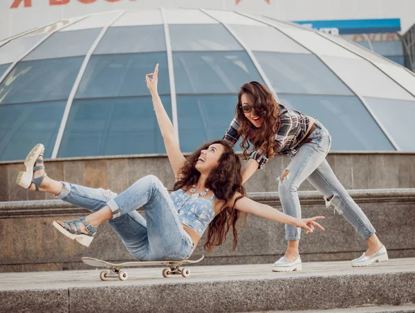 İki genç kız açık havada kaykay ile eğleniyor