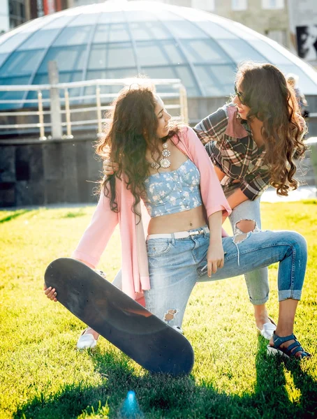 Yeşil çimenlerin üzerinde poz kaykay ile rahat kıyafetler'de iki genç karışık yarış kız