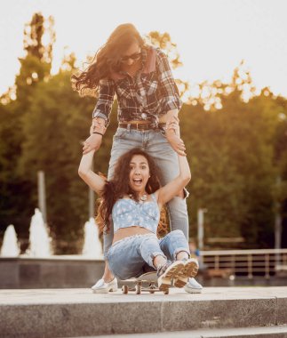 İki genç kız açık havada kaykay ile eğleniyor